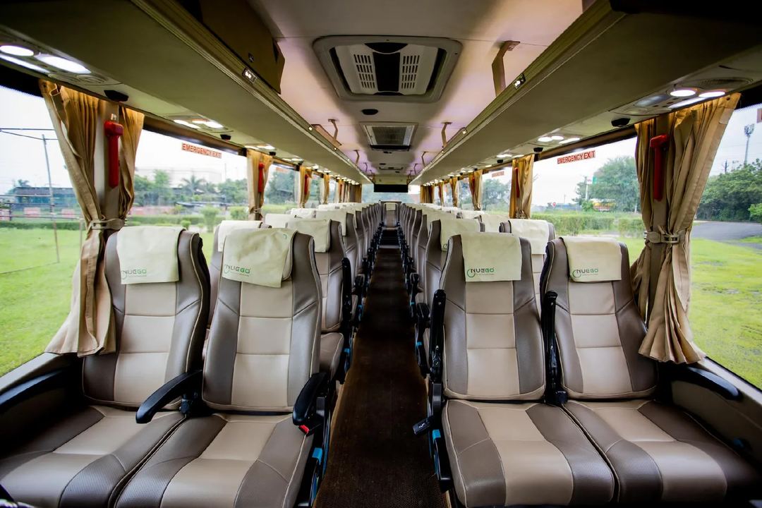 Wide view down the aisle of a clean NueGo intercity coach with reclining seats, overhead lighting and marked emergency exits.
