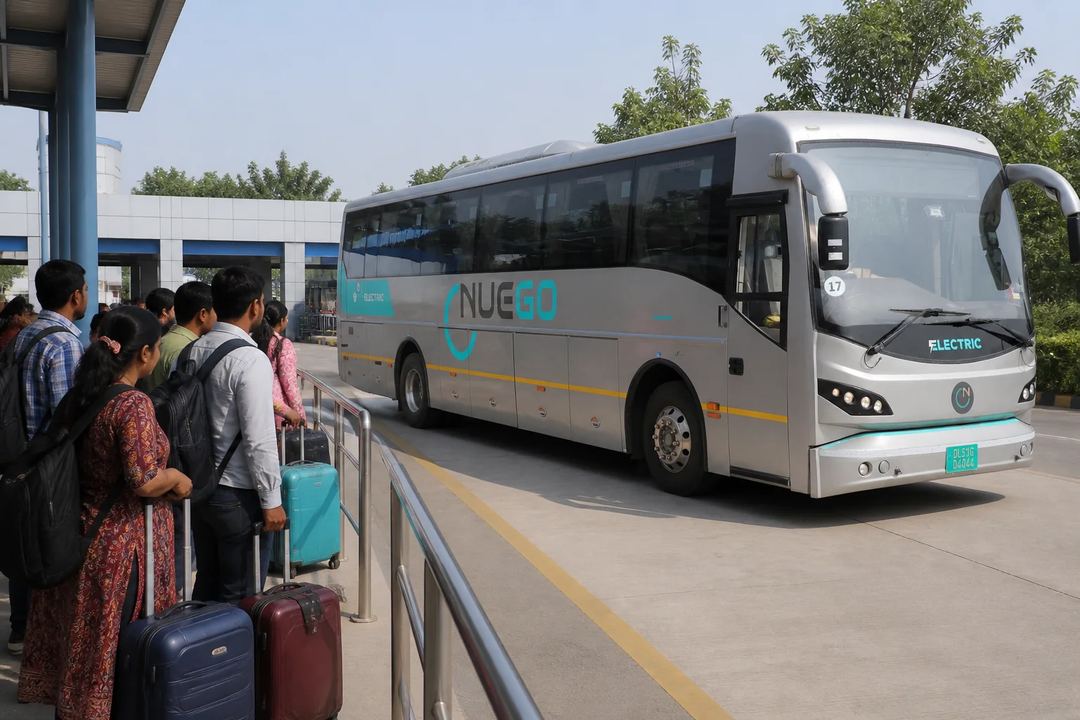Passengers waiting behind a barrier at a terminal while a NueGo electric coach approaches its bay.