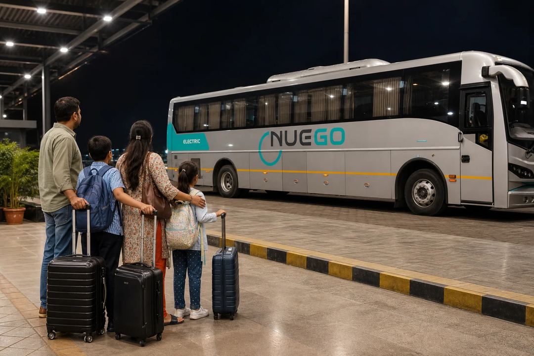 A family waits together with luggage in a well-lit terminal at night while a NueGo coach stands at the bay.