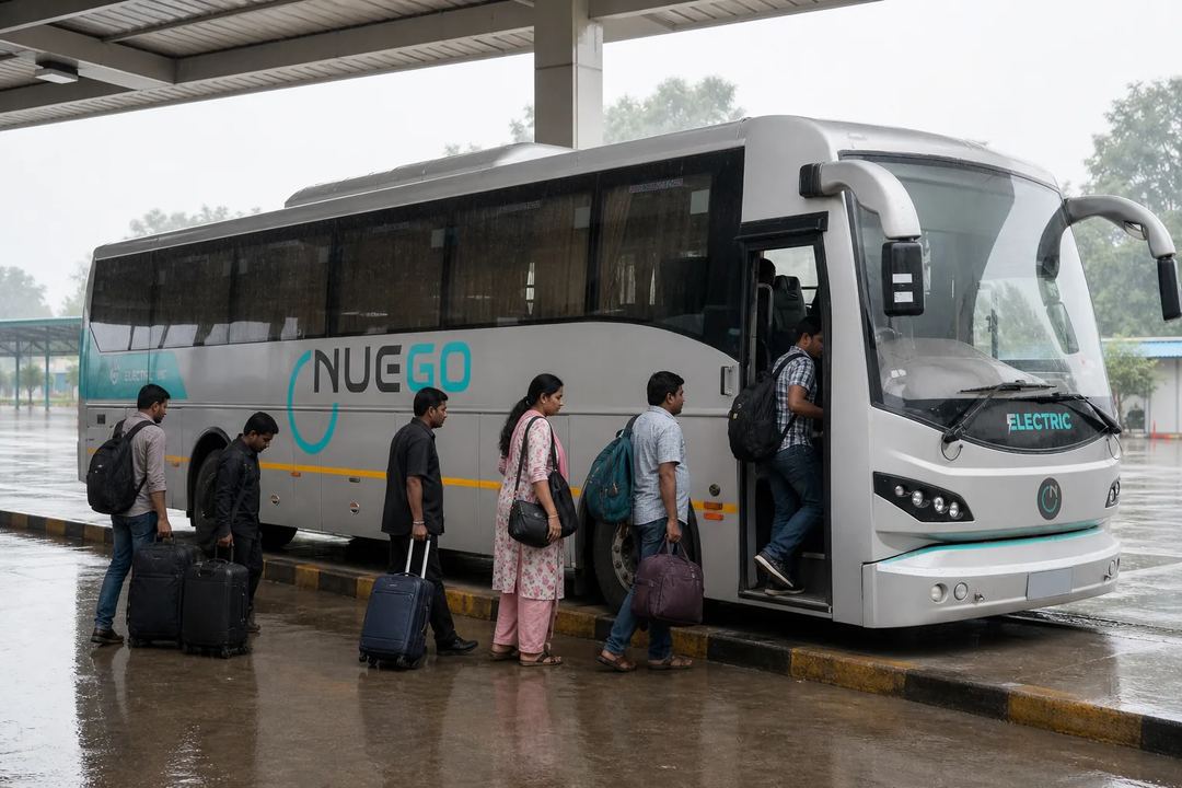 Travellers boarding a NueGo electric intercity coach at a covered bus bay during light monsoon rain in India.