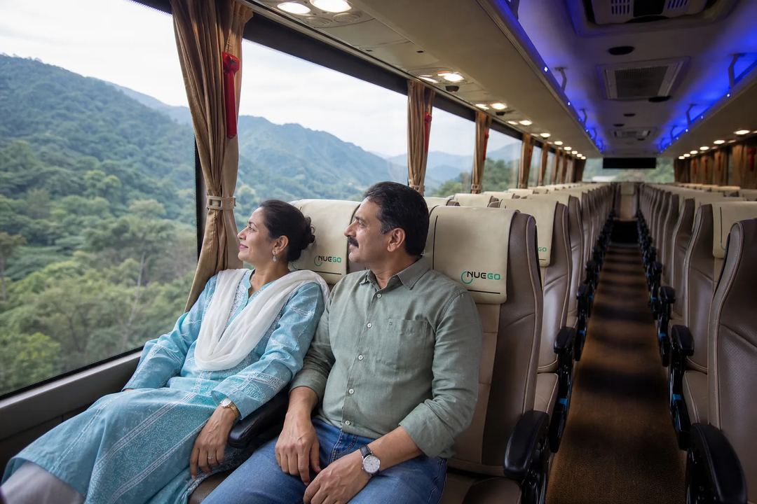 Couple seated together inside a NueGo electric intercity coach on the Delhi–Rishikesh route, looking towards the hills.